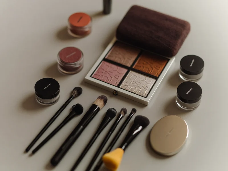 Trousse de maquillage organisée : pinceaux, palettes, éponges et pots sur une table claire